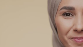 Middle eastern beauty. Half face portrait of young happy muslim lady smiling widely to camera, posing over beige studio background, empty space, slow motion