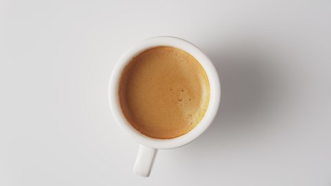 Cup of fresh aromatic coffee with crema, top view, rotate on white background.