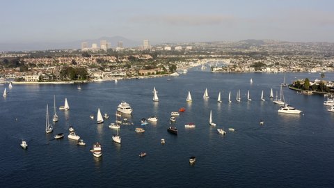 Aerial Reversing Over Sailboats In An Idyllic Harbor With A City In The Background - Newport Beach, California