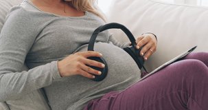 Keeping baby entertained. 4K footage of a woman holding headphones over her pregnant belly.