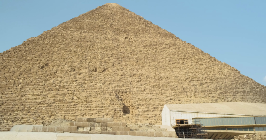 long haired caucasian girl in sunglasses and white dress walks past the Great Pyramid of Giza in Cairo Egypt. Hands apart, clear day, wide shot, slow motion