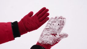 Close-up view slow motion 4k stock video footage of cute snowy red gloves on hands of woman standing outdoors in snowy park background. One glove is clean and dry another wet and snowy