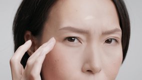 Closeup Shot Of Middle Aged Japanese Woman Touching Eye Wrinkles Looking At Camera Having Nystagmus Problem Posing On Gray Studio Background. Facial Skincare For Aging Skin. Cropped
