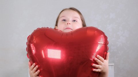 little cute girl in a red dress gently hugs red heart shaped balloons with her hands. valentines day concept