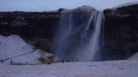 Tourists Admiring Breathtaking Waterfall Seljalandsfoss On A Windy Winter Sunset In Iceland. wide