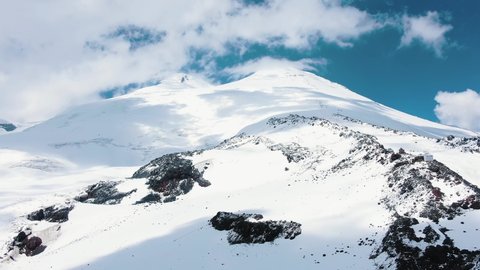 Fantastic cinematic panorama of the high snowy mount Elbrus in the Caucasus mountains against the blue sky, aerial view of glaciers and rocks