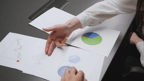 Business analytics concept. Unrecognizable colleagues or partners discussing financial development and marketing strategy with graphs and charts on table at office, top view, slow motion - Powered by Shutterstock - Get 15% off with code: PIKWIZARD15