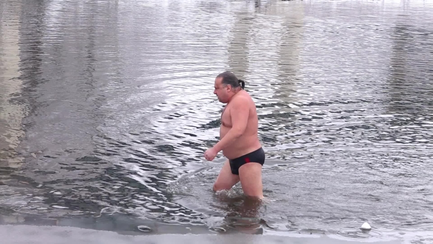 A man comes out of the water after swimming in a winter river against the backdrop of a winter forest.