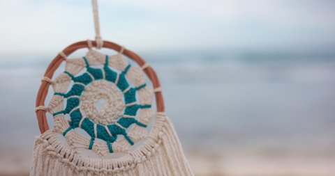 Close-up of beautiful blue and cream color woven dreamcatcher slowly swinging with background. Traditional handicraft hanging with blurred horizon in the distance. Holidays and decoration