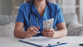 Hospital accounting. Medical invoice. Financial report. Unrecognizable female doctor counting money us dollars banknotes cash filling record. - Powered by Shutterstock - Get 15% off with code: PIKWIZARD15
