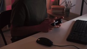 Cyber addiction. Gaming man. Night entertainment. Unrecognizable guy playing on computer with gamepad sitting dark light home interior.