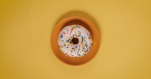 Donut on plate on yellow background table gets eaten. Retro, vintage indie scene filmed top view, plan view from above. Stop motion animation. Circular round object.