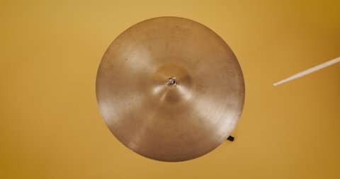 hand with drumstick hit and play cymbal on yellow background floor. Retro, vintage indie scene filmed top view, plan view from above. Warm sunflower, mustard color. Close up Circular instrument..