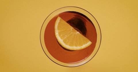 lifting up red drink rose with lemon orange slice on yellow table. put down. Retro, vintage indie scene filmed top view, plan view from above. Warm sunflower, mustard color. Circular round object.