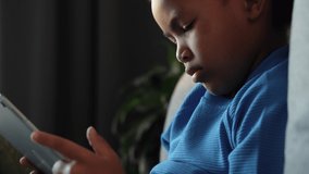 Close up serious cute african little boy sitting at sofa, using tablet computer, looking seriously thinking. online education via internet, play games, beautiful mixed races child. 4k footage