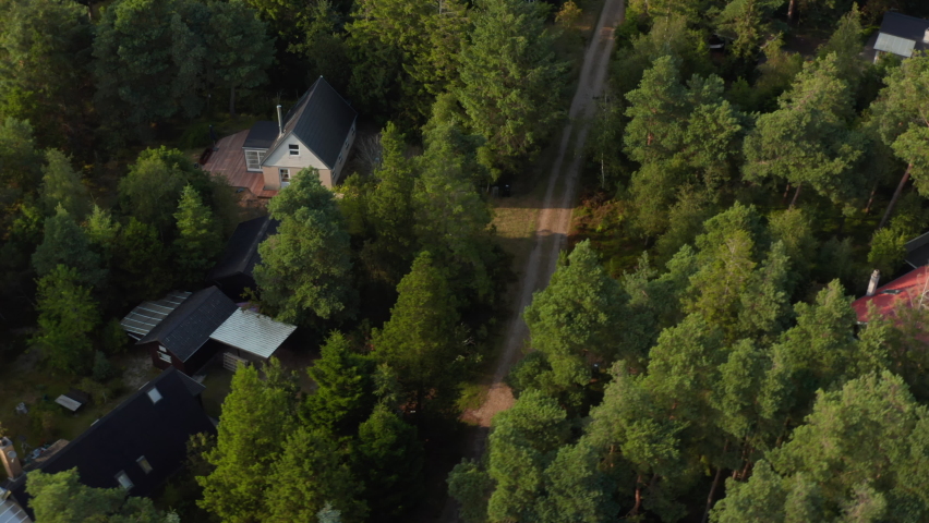High angle view of vacation houses between trees. Coastal landscape against low sun. Tilt up reveal of sea coast. Denmark