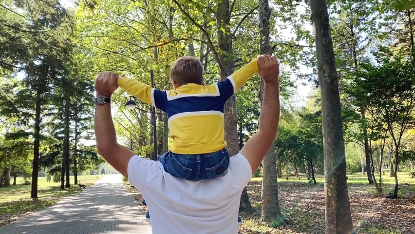 Father and son walking in city at sunset. Two year old kid is sitting on the parent