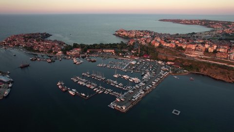 Drone view of Sozopol port enriched with bunch of boats and many building in the back, in the seaside town, Sozopol. Summer sunset from above