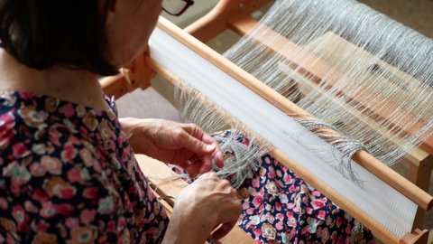 Woman with heddle hook in her hand is warping a weaving handloom. Threading the table loom. Start of the weaving