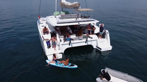Phuket, Thailand, 20, December, 2019:
Tourists are resting on a sailing catamaran, two girls rode a SUP board and arrived back on board