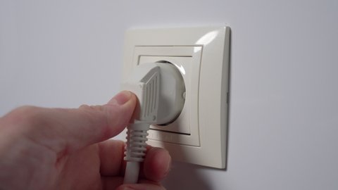 Plugging power electrical plug in electric socket on a white home wall. Connecting close up. Household electricity concept