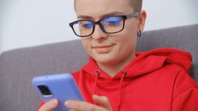 Beautiful white woman in glasses using modern smartphone. Pretty young adult female with short hair wearing red hoodie browsing internet news feed on mobile phone in 4k stock video clip