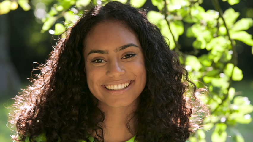 Beautiful biracial African American girl teenager young woman outside smiling, laughing and turning to camera standing under a tree | Shutterstock HD Video #1086397682