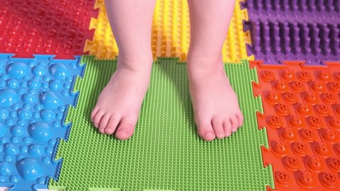 The child does exercises on the orthopedic mat, legs close-up.