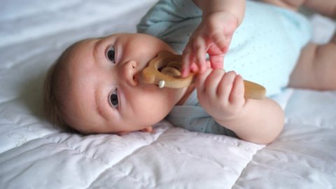 cute newborn three month old baby, with a wooden natural rattle, lies on the bed, Teething concept, childcare and parenthood., close-up, top view