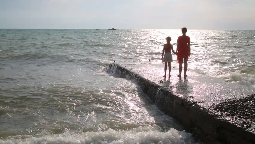 Mother and daughter watches the sunset over the sea while standing on the concrete pier
