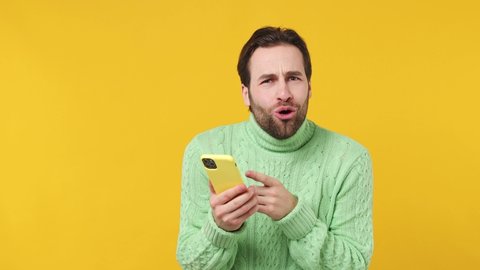 Fun young brunet bearded man 20s wears mint shirt hold use mobile cell phone typing browsing swipe chatting send sms doing online shopping booking tour isolated plain yellow background studio portrait
