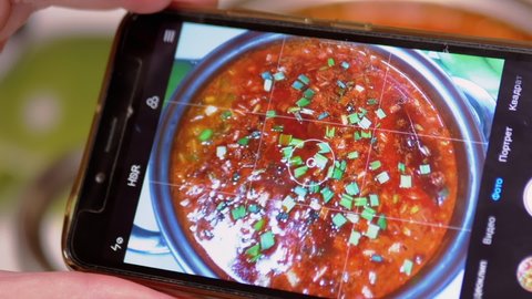 Female Hands Taking a Picture on a Smartphone Traditional Ukrainian Red Borscht. Photo of food through the camera of a mobile phone in an application. Photographing food. Lunchtime. Home kitchen.