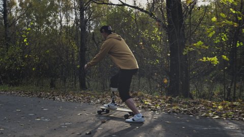 A young man with a metal prosthetic leg rides a skateboard in an autumn park. Go in for sports with an artificial leg. a11y