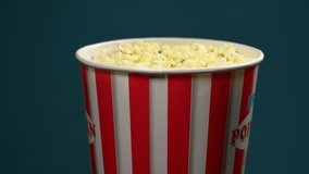 Close-up side view slow motion 4k video footage of hot tasty popcorn snack in paper striped red and white big bucket isolated on dark background turning around slowly