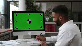 Mock-up, green screen, chroma. Concentrated manager or business owner sit at desk in office, wearing white shirt, listening online business training, watching coach video, taking notes,improves skills
