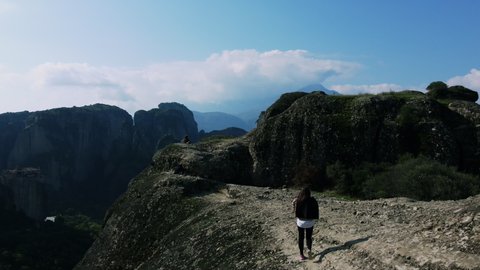 Girl's walking among the Meteora hills in Greece. Picturesque view on ancient temples monasteries. Drone flies.