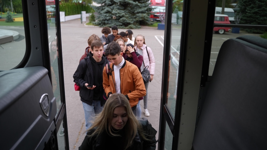 Closeup of multinational secondary school pupils taking turns entering school bus to go home after studies, shoot from inside bus. Queue of diverse high school students boarding school bus after class Royalty-Free Stock Footage #1086417272