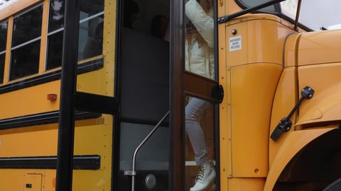 Close-up of multiracial teenage high school students walking down steps of school bus rushing to class. Multi-ethnic secondary school pupils leaving doors of yellow school bus arriving to studyの動画素材