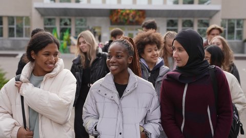 Group of happy high school students chatting while walking through school park after studies. Three multi-ethnic schoolgirls, indian, african american and arab female in hijab talking and smiling Arkivvideo