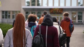 Rear view of multi-ethnic secondary school pupils with backpacks walking to school building for lessons. Group of multiracial teenage schoolkids outdoor on the way to high school - Powered by Shutterstock - Get 15% off with code: PIKWIZARD15