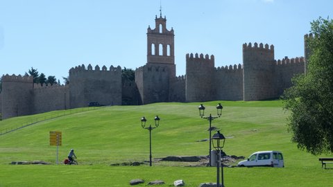 Avila, Spain - June 28, 2021: Busy road and fortified walls surround the medieval spanish city of Avila on background, sunny daytime view against blue clear sky. Castile and Leon. UNESCO. Spain