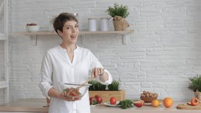 A female blogger holds a glass bowl with vegetable salad in her hands, shoots a video tutorial on cooking, a young woman at home in the kitchen tells a recipe on camera