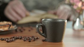 Hot coffee in a mug, steam rises above the cup, backlight. Lunch in a cafe, a man flipping through an old book at a wooden table. Close-up, selective focus, 4K footage in real time. - Powered by Shutterstock - Get 15% off with code: PIKWIZARD15