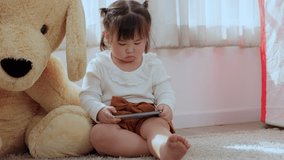 Cute Asian little girl holding smartphone enjoying using smartphones listening to music and playing games at home. Internet of thing and mobile technology concept.