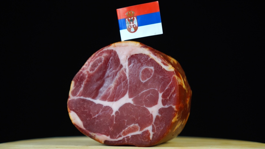 Delicious smoked tenderloin with small flag of Serbia, piece of meat rotating on balck background.