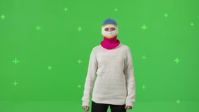 Close-up of young woman wearing knitted mask hat dancing on a green screen background. Attractive girl making content for social media. Modern blogger creating a master class. Chroma key