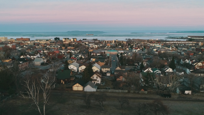 A small city sits placed against a large body of water with mountainous islands and a cool evening sky above the horizon.