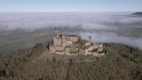 Old fairytale castle on the hill. Misty clouds on background
