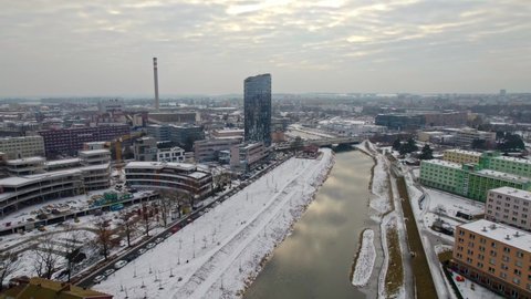 Aerial drone shot over snow covered Olomouc city in Moravia region of Czech Republic with beautiful modern buildings and bridge over the river passing by on chilly winter evening.
