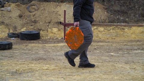A shooter carries a metal gong around the shooting range, movement from left to right, it is raining, the camera moves, focus on the metal gong, medium shot, soft focus
